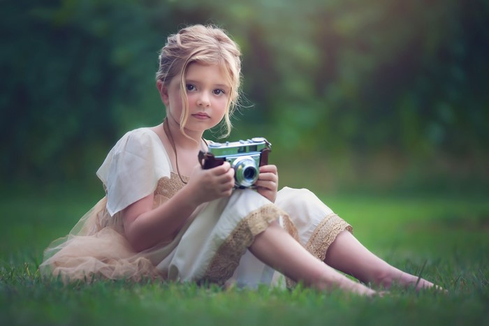 Little girl with a camera sitting in grass