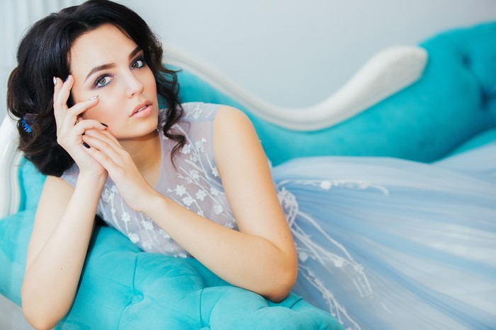 Brunette girl in a blue dress on a turquoise couch