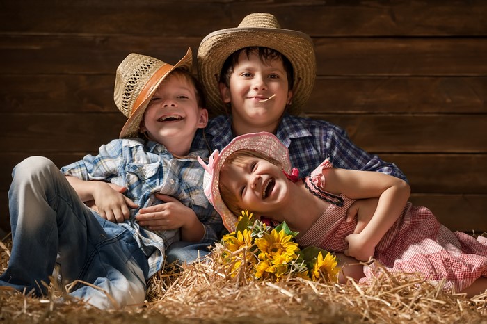 Three children in cowboy hats on hay with sunflowers