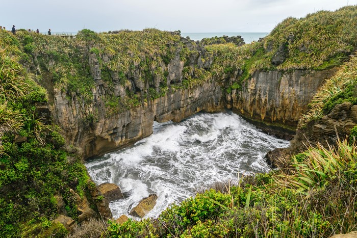 Waves crashing into a rocky cove in Paparoa National Park, New Zealand