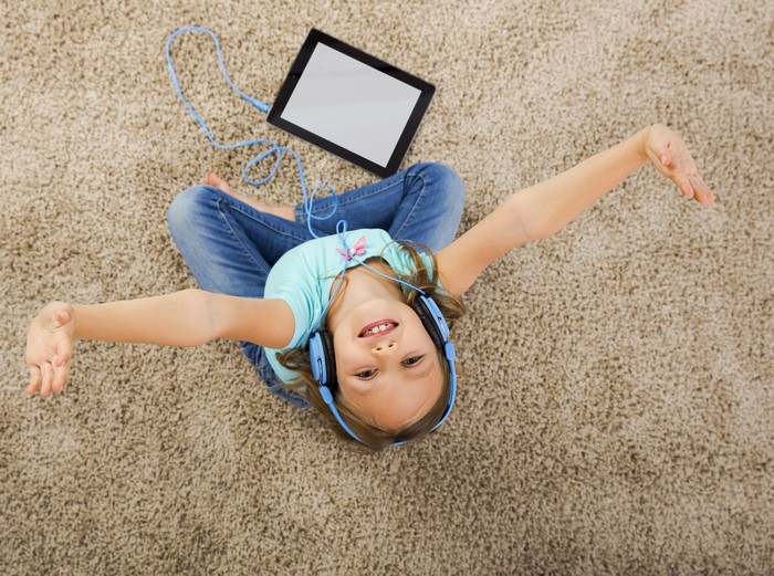 Girl with headphones and tablet on carpet