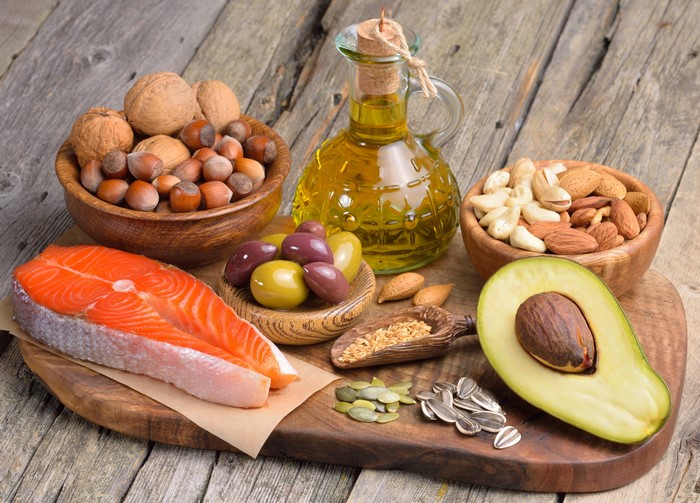 Still-life of healthy foods including salmon, nuts, avocado, and olive oil