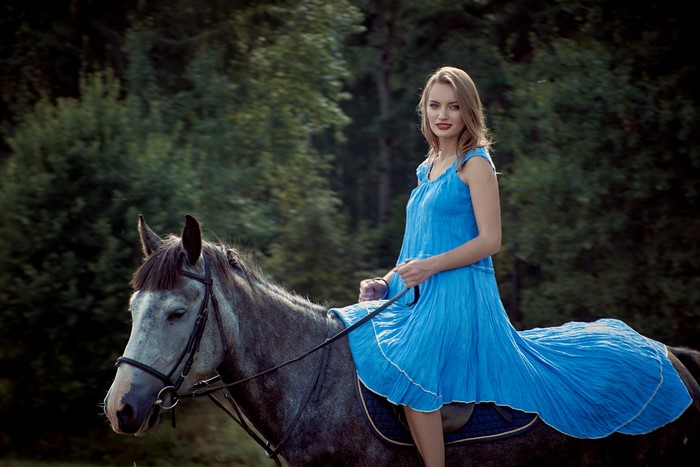 Blonde girl in blue dress riding a horse