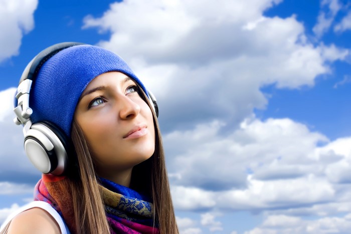 Girl with headphones and winter hat against cloudy sky