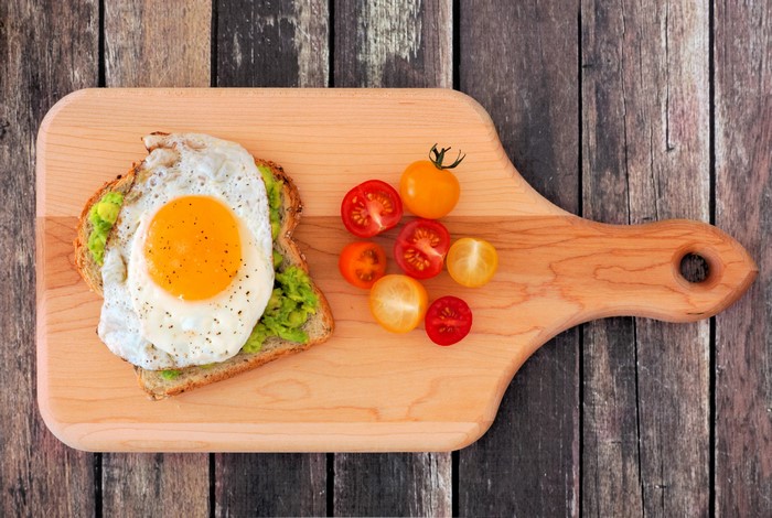 Avocado toast with fried egg and cherry tomatoes on cutting board