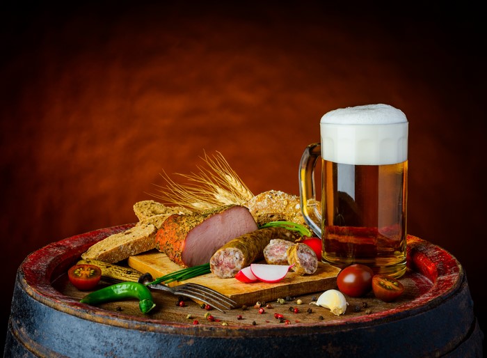 Still-life of beer, ham, sausage, and bread on a barrel