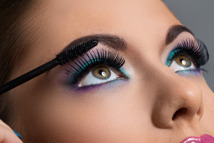 Woman applying mascara to her eye with colorful makeup