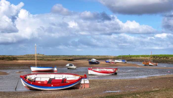 Boats moored on a tidal estuary under a cloudy sky in Norfolk, UK