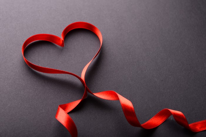 Red ribbon in heart shape on dark background