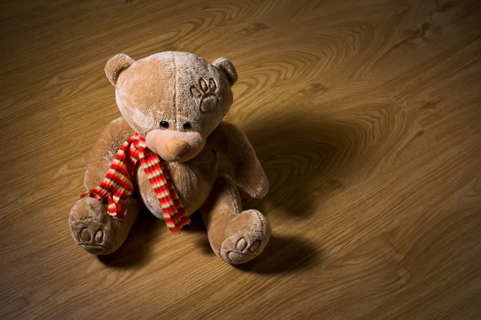 Teddy bear with scarf sitting on wooden floor