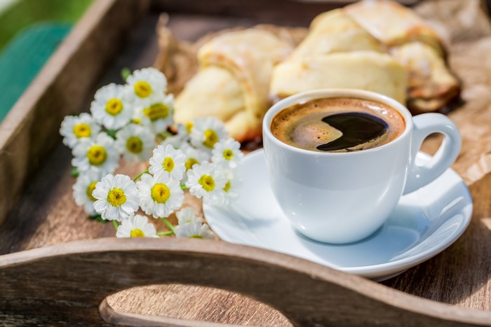 Coffee cup with pastries and chamomile flowers on a tray