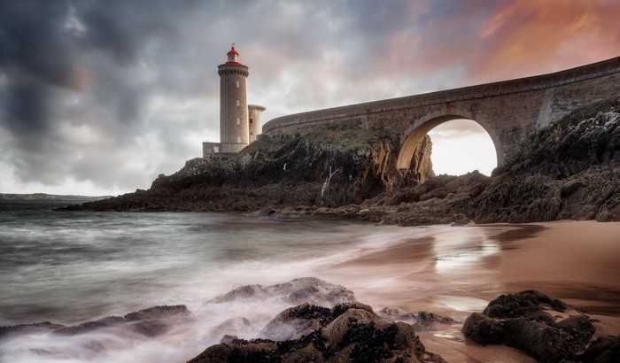 Lighthouse and bridge over rocky coast at sunset