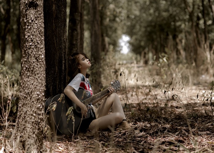 Asian girl sitting with guitar in forest