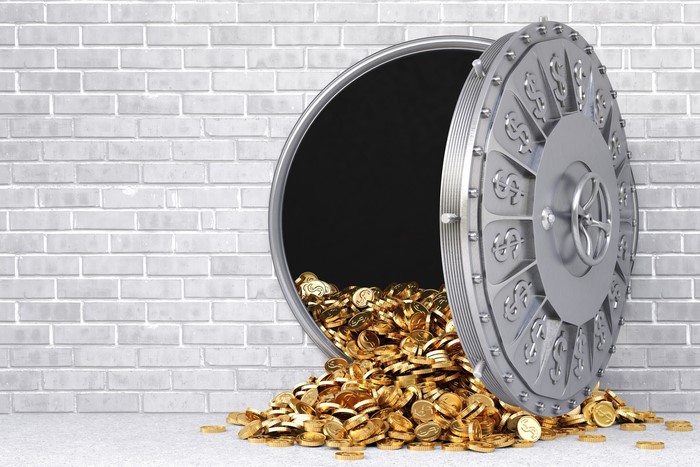 Vault door overflowing with gold coins in front of a brick wall