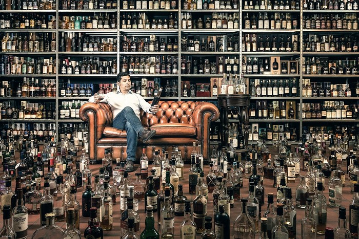 Man sitting on a leather sofa surrounded by bottles