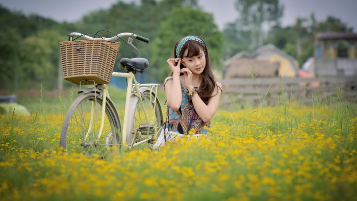 Asian girl with bicycle in a field of yellow flowers