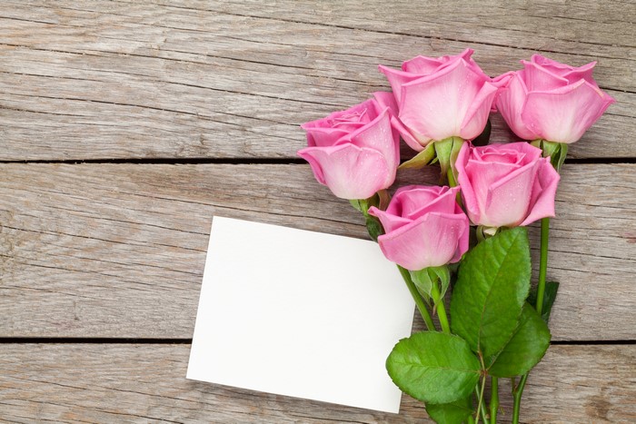 Pink roses and blank card on wood planks