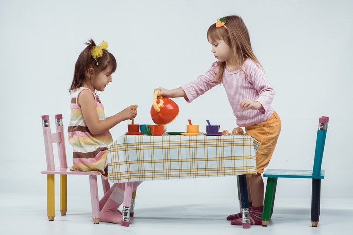 Two little girls playing tea party with kettle and table