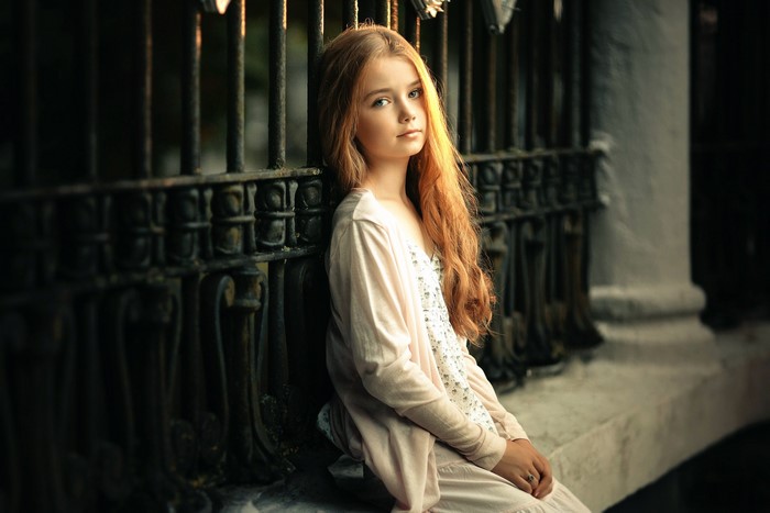 Young girl with long red hair leaning on a fence