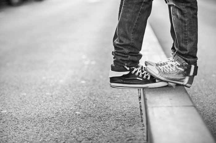 Close-up of legs wearing jeans and sneakers standing on a curb