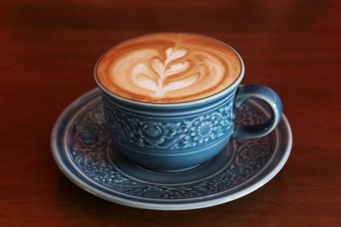 Blue ceramic cup of cappuccino with latte art on saucer