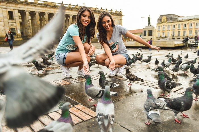 Two women feeding pigeons in a town square