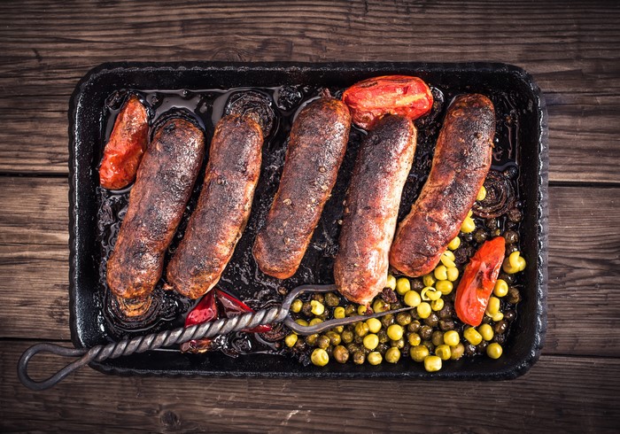 Roasted sausages with tomatoes and peas in a pan