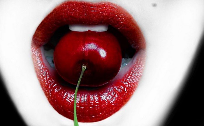 Close-up of red lips holding a cherry