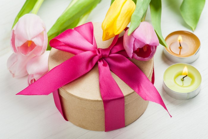 Gift box with pink ribbon and tulips, lit candles