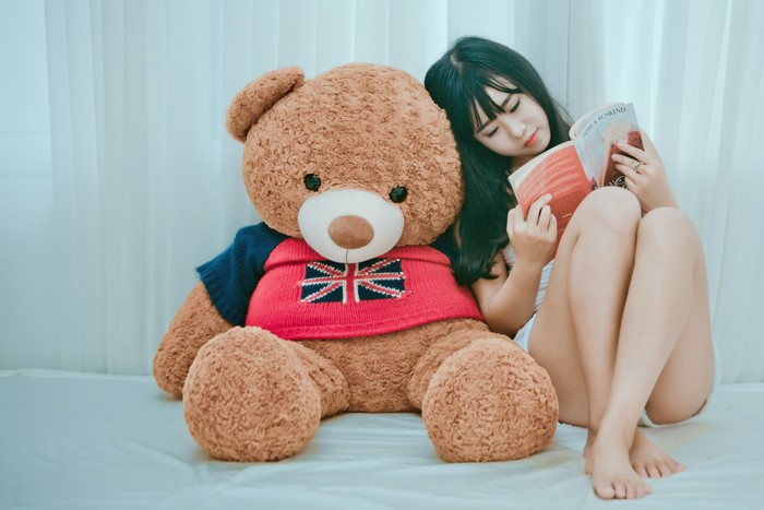 Asian girl reading a book next to a teddy bear