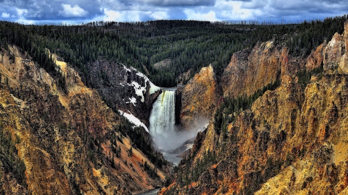 Waterfall in a canyon with pine forest and cloudy sky