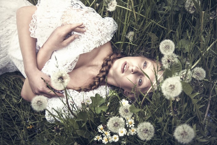 Woman with braid in white lace dress lying in dandelions