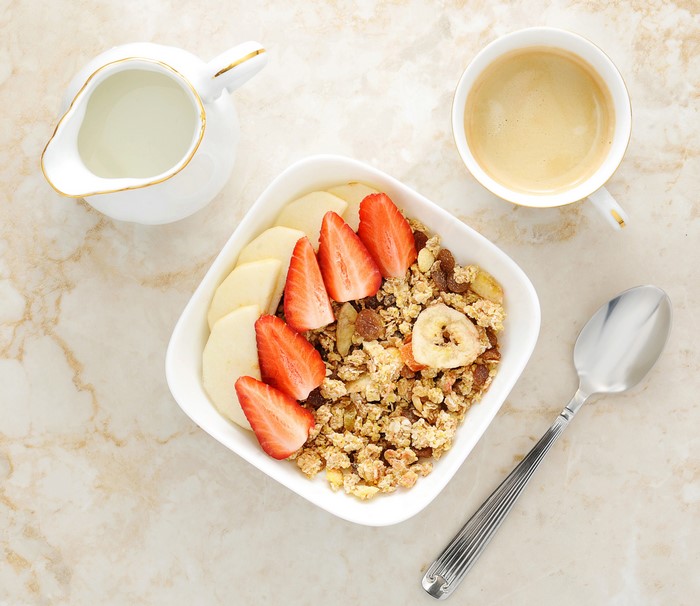 Muesli with strawberries, apple, banana chips, coffee, and milk
