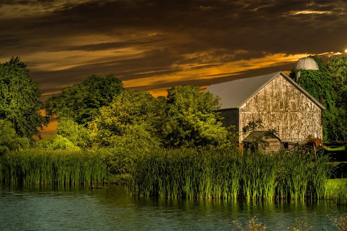 Barn and silo by a pond at sunset
