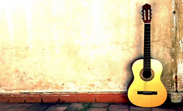 Acoustic guitar leaning against a textured wall