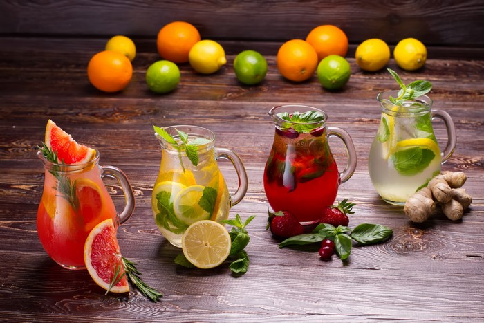Four pitchers of fruit infused drinks with citrus fruits and berries