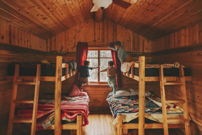 Three boys in a wooden cabin looking out a window