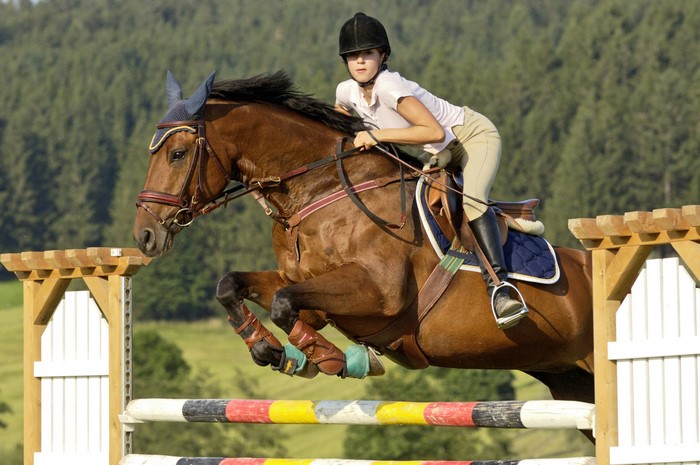 Girl riding a horse jumping over a fence