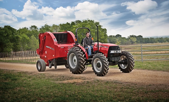 Man driving a red Case IH Farmall 65A tractor with a baler