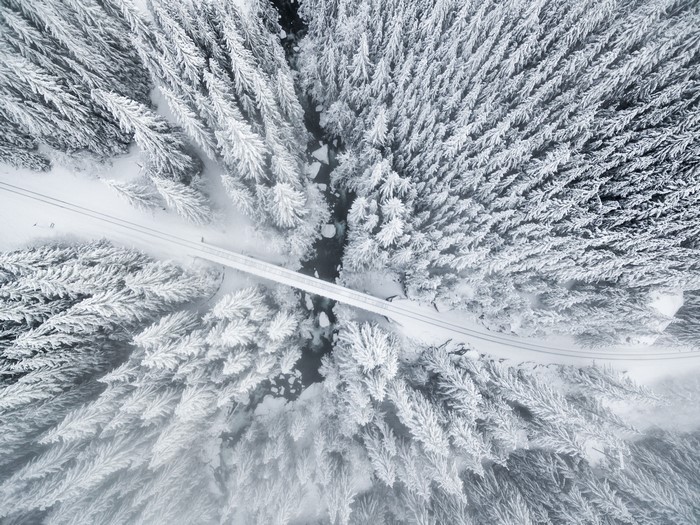 Aerial view of a snow-covered forest with a bridge over a river