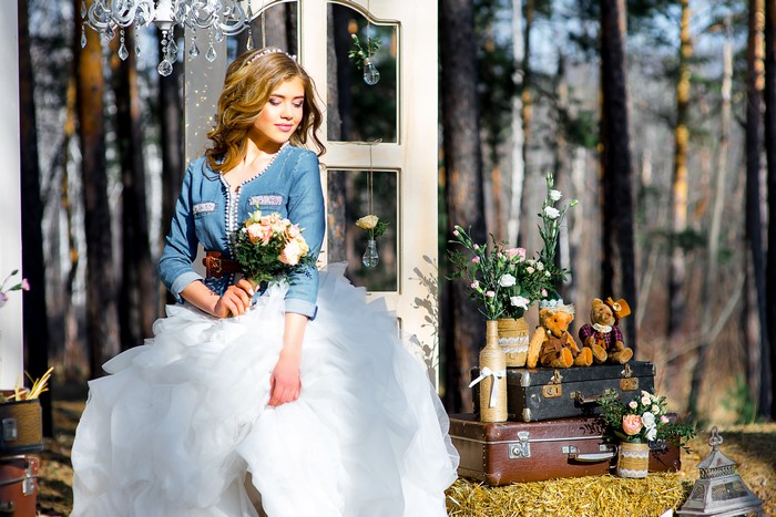 Bride in denim jacket holding bouquet with teddy bears and suitcases