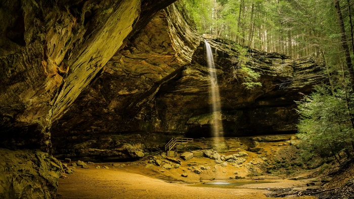 Waterfall cascading into a cave with wooden stairs