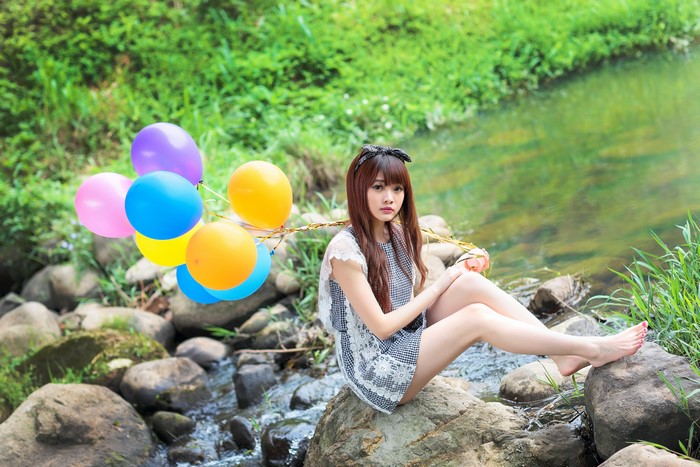 Asian girl with balloons sitting by a stream