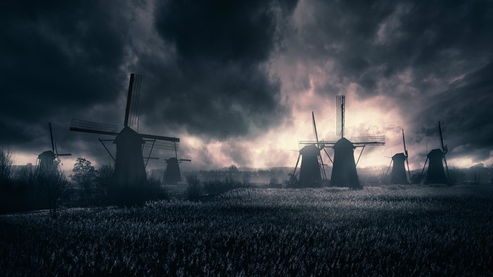 Several windmills in a field under a stormy sky