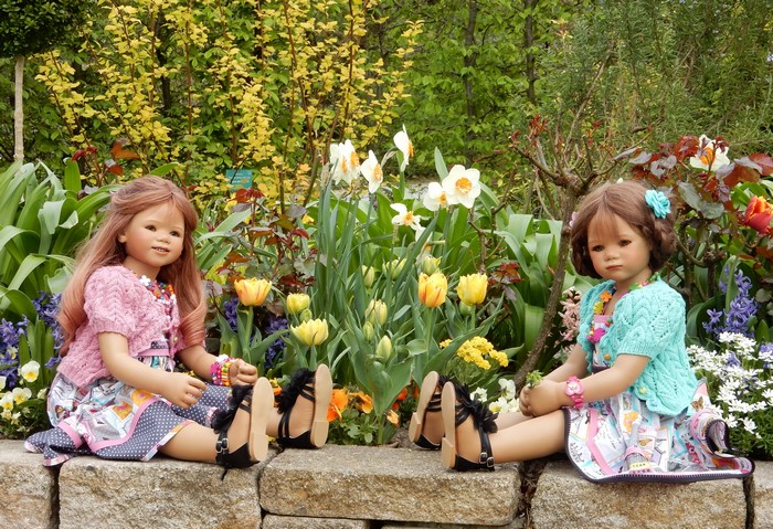 Two dolls sitting in a garden with tulips and daffodils
