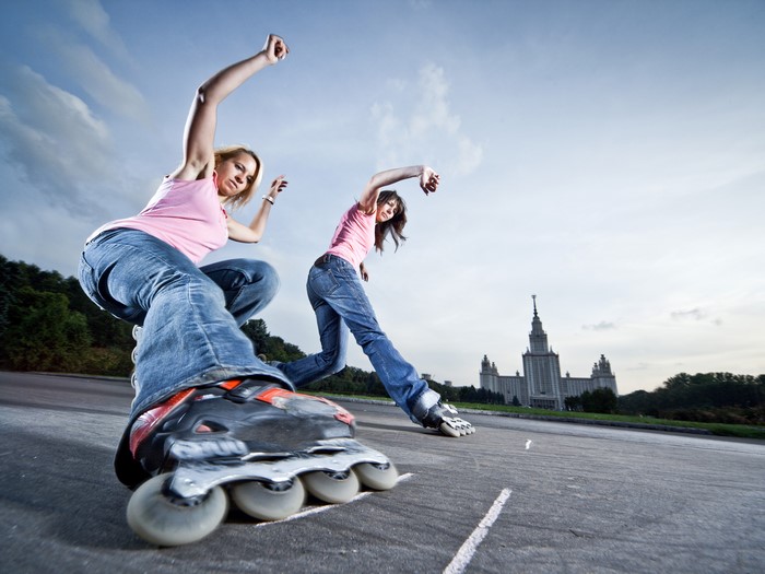Two girls roller skating with a building in the background