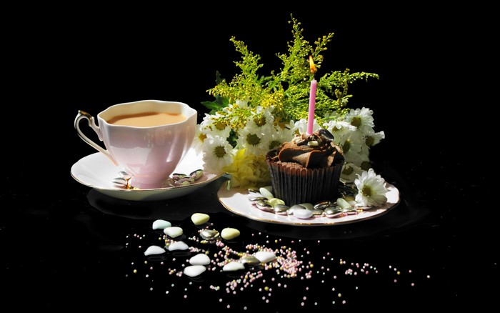Cup of coffee with a cupcake and flowers