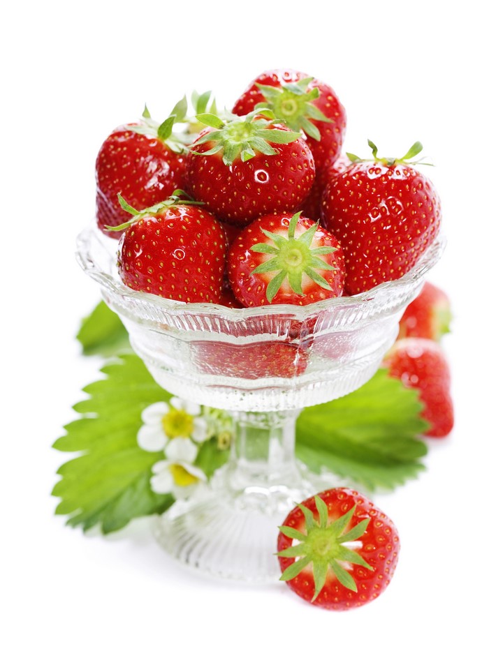 Strawberries in a glass bowl with leaves and flowers