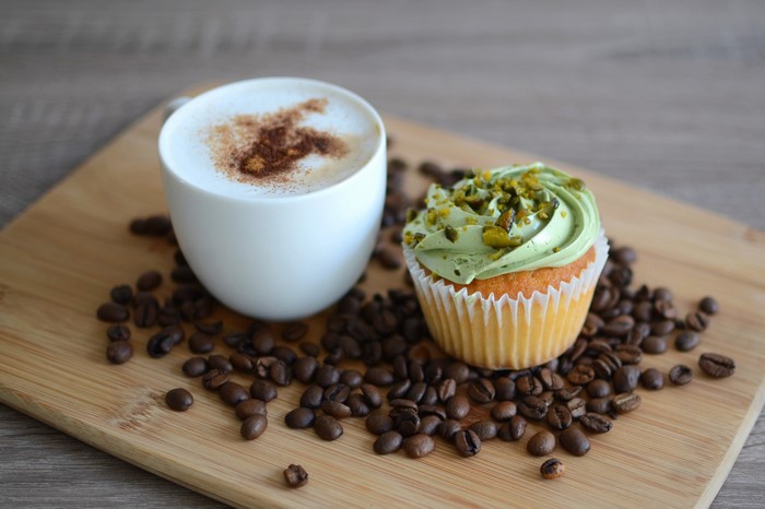 Cappuccino and pistachio cupcake on a cutting board with coffee beans