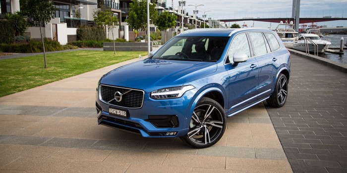 Blue Volvo XC90 parked by a waterfront with modern buildings